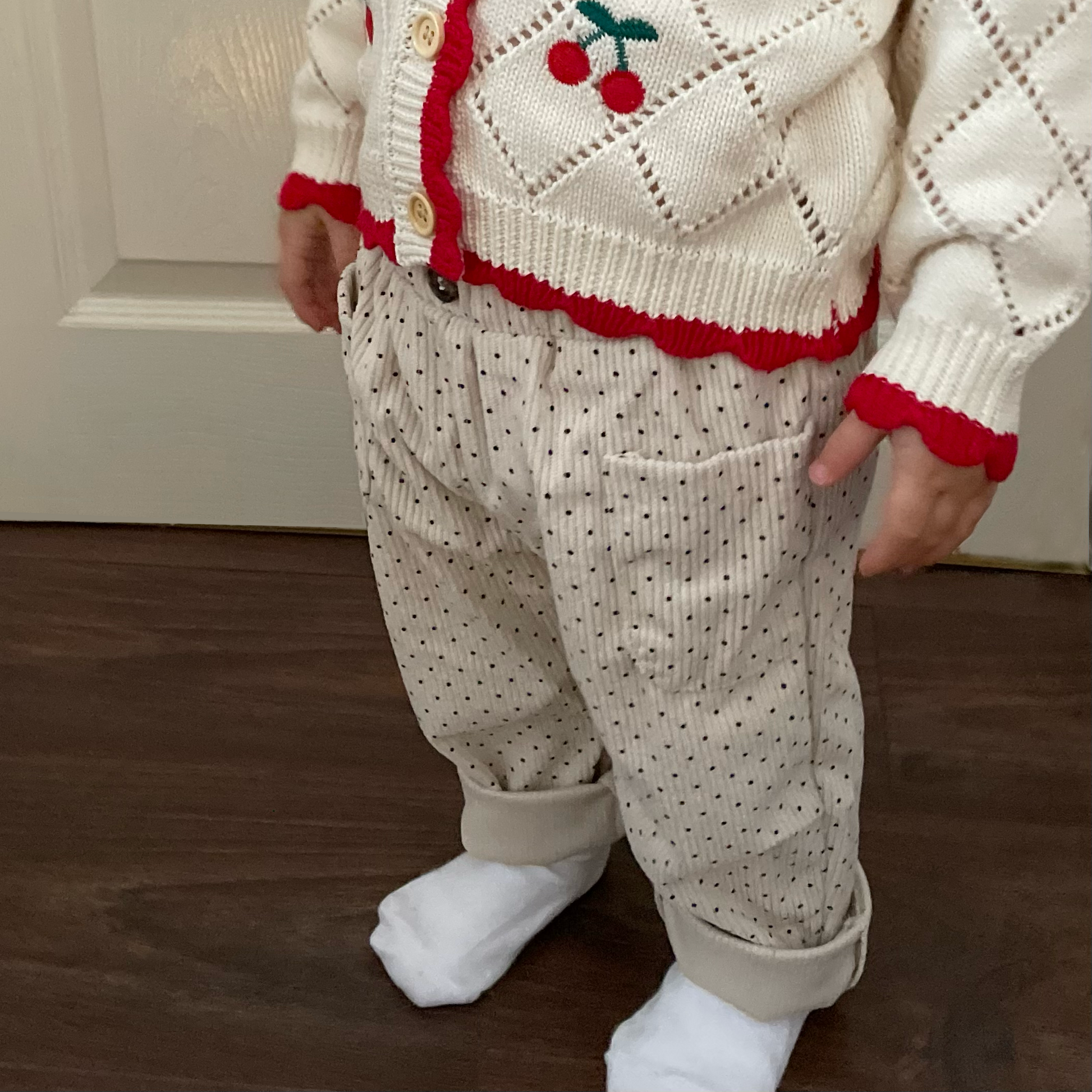 Toddler wearing cream polka dot baby corduroy trousers with rolled leg cuffs. Paired with cherry baby knit cardigan