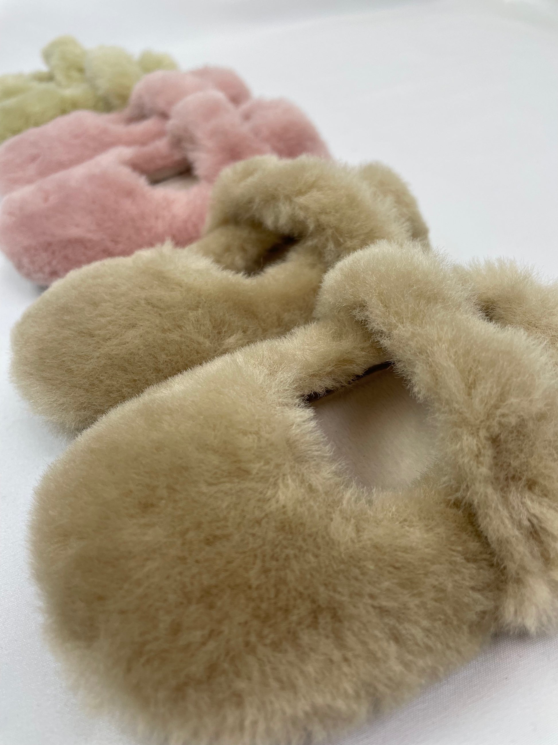 Fluffy baby slippers with apricot brown slipper in foreground, pink slipper next to it and green slipper in the background