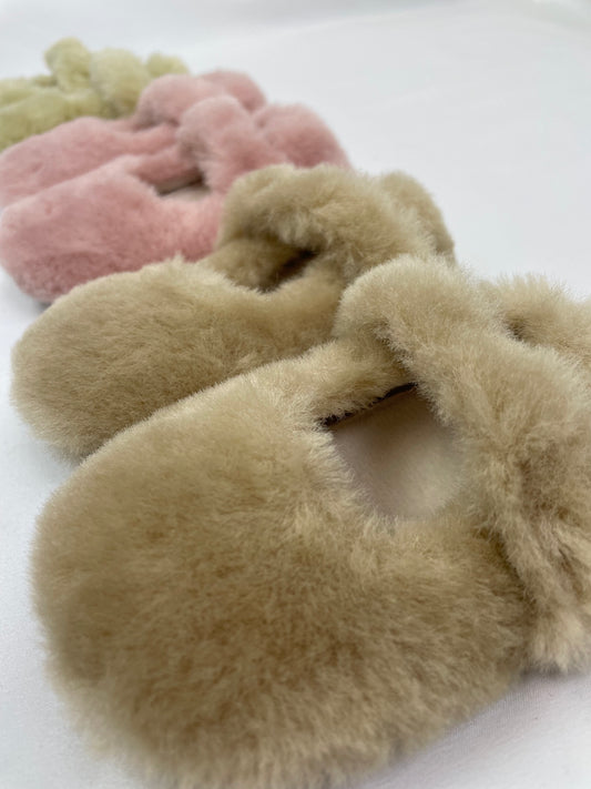 Fluffy baby slippers with apricot brown slipper in foreground, pink slipper next to it and green slipper in the background