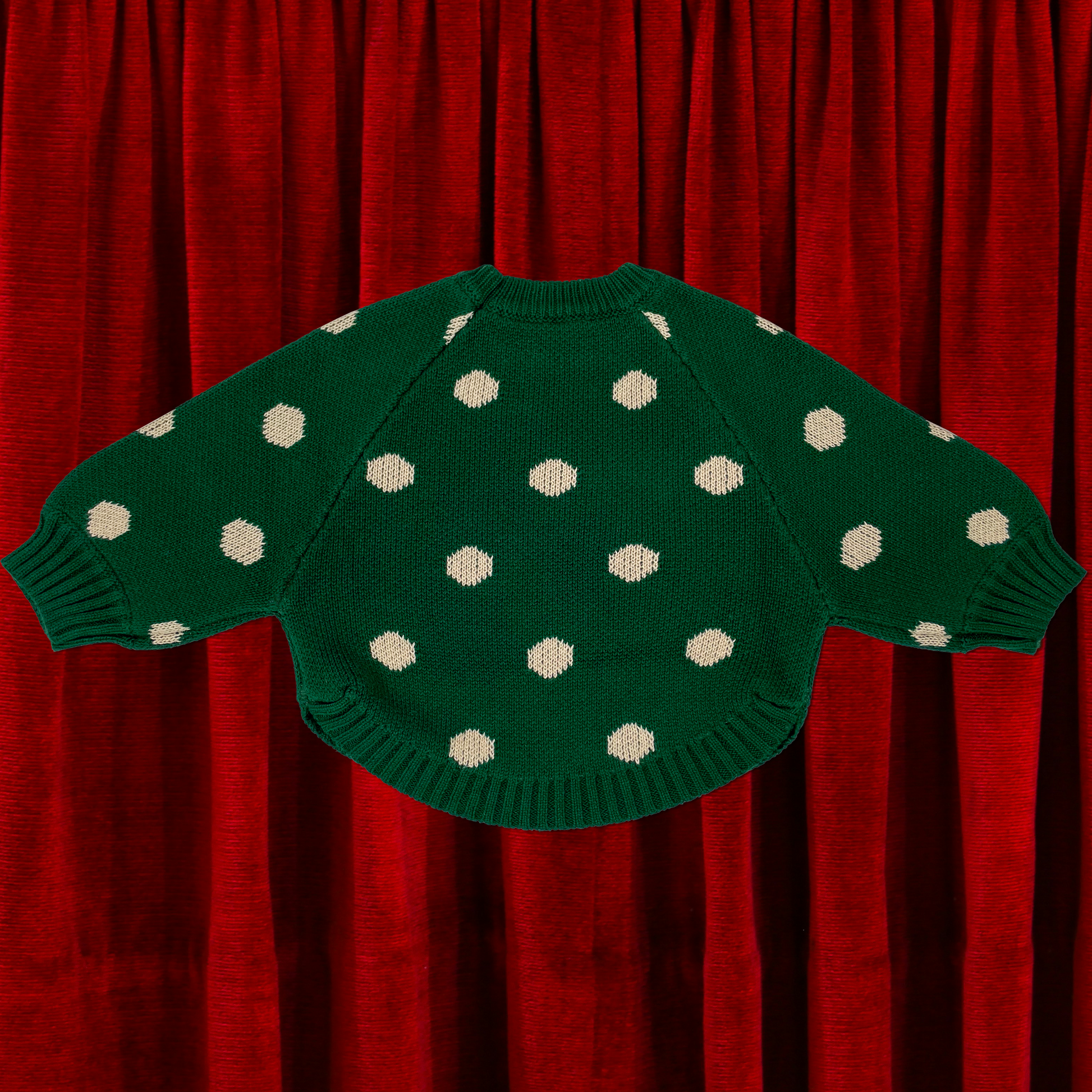 Green knit jumbo spot baby jumper laid flat to show back view raglan sleeves and curved hem