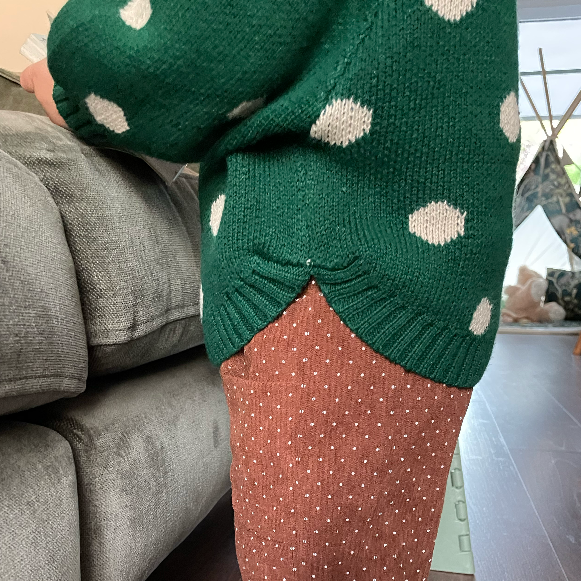 Green jumbo spot baby jumper worn by toddler standing with side view to show curved hem detail