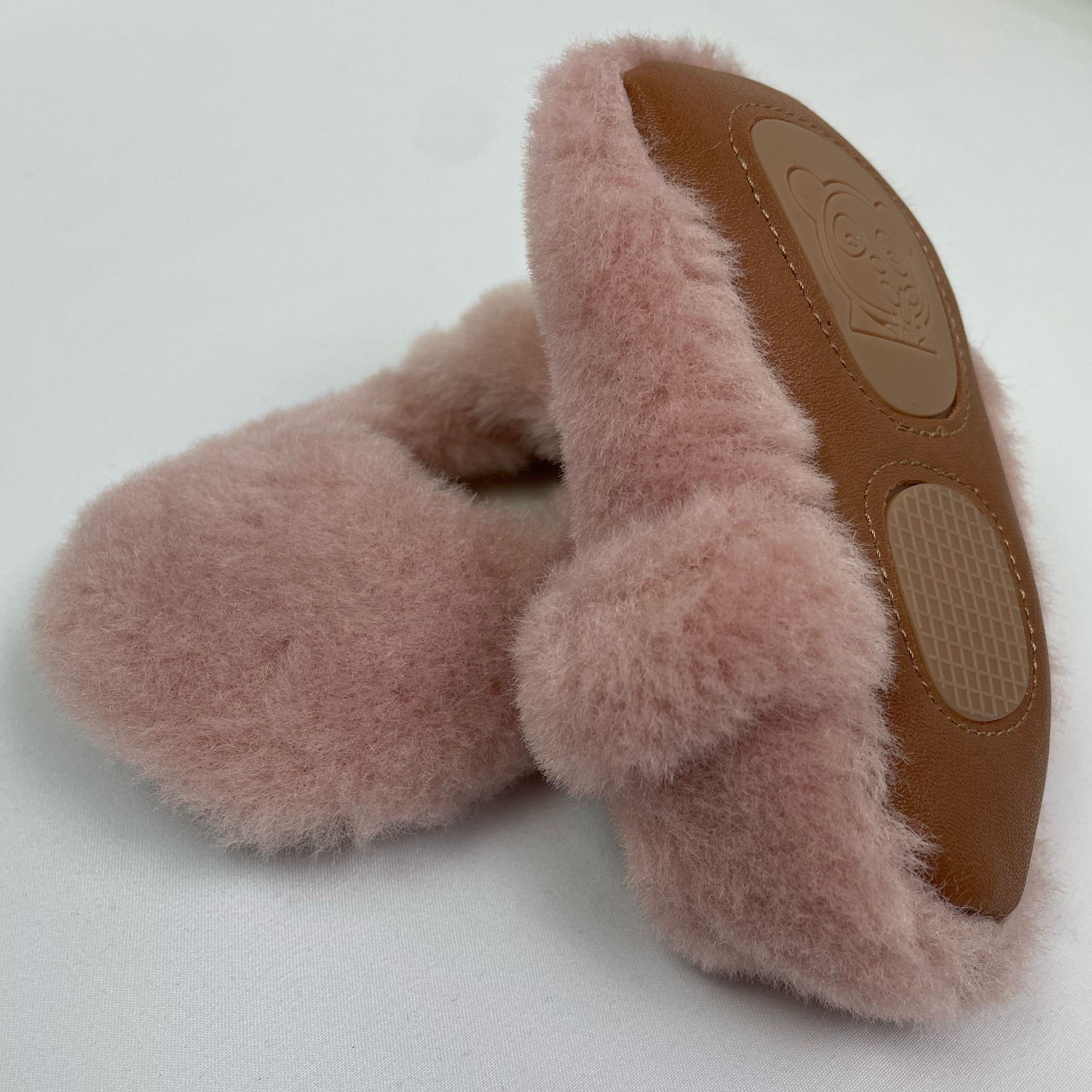 Pink fluffy baby slippers with one slipper showing the flexible rubberised anti slip sole