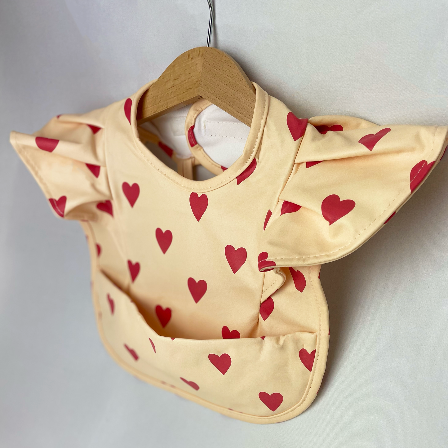 Baby weaning bib. Beige with red hearts. Bib with pocket. Wipeable surface. Frill shoulders.