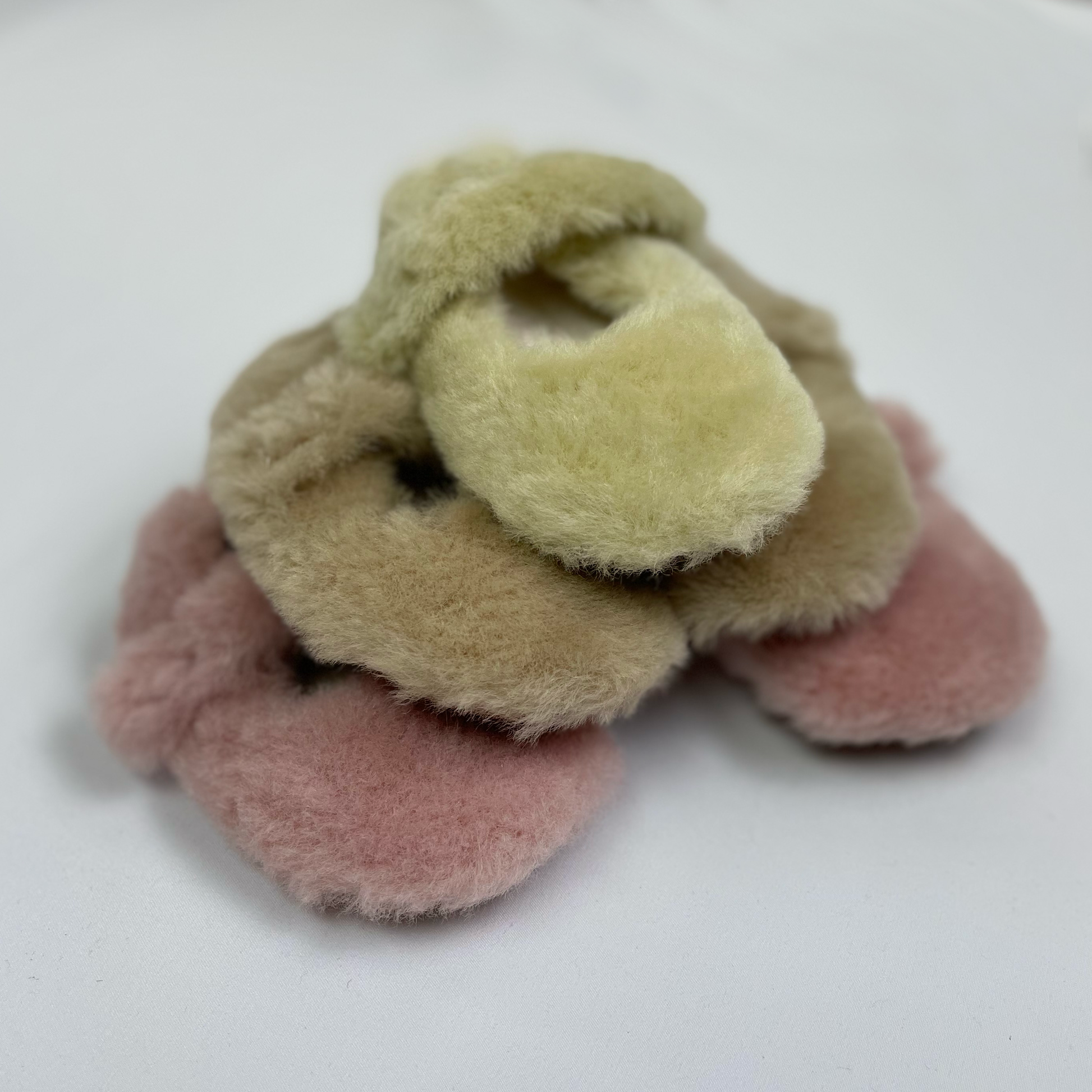 Fluffy baby slippers stacked in a pile with green on top, apricot beige in the middle and pink on the bottom