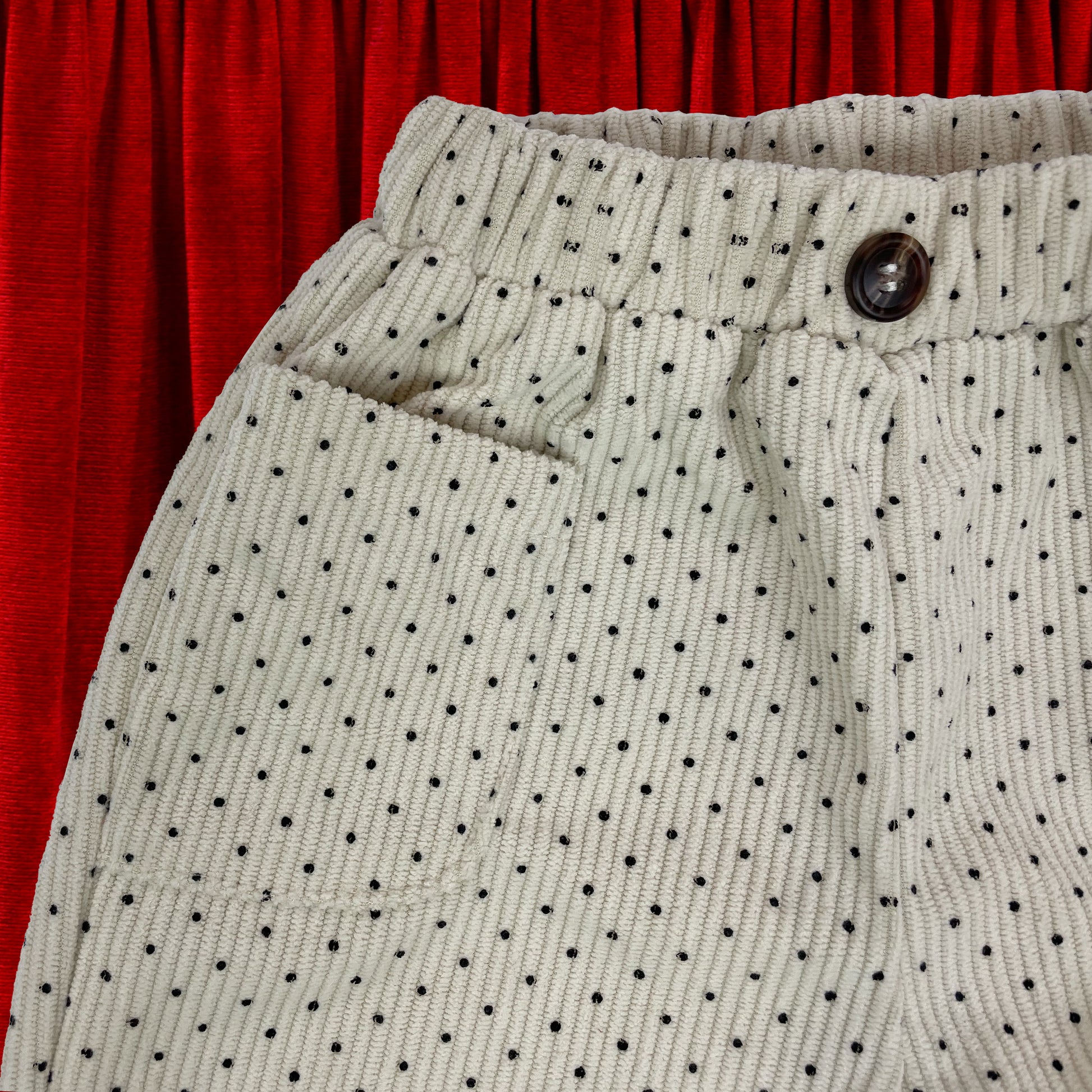 Cream polka dot baby toddler trousers close up of front shows hip pocket and elasticated waist with button. Fabric looks soft and warm.